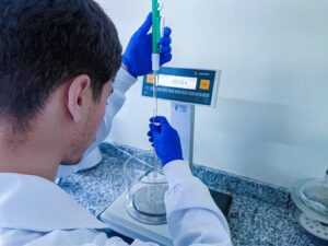 Analista de laboratório realizando calibração de precisão com balança analítica Sartorius e pipeta graduada para medições metrológicas.