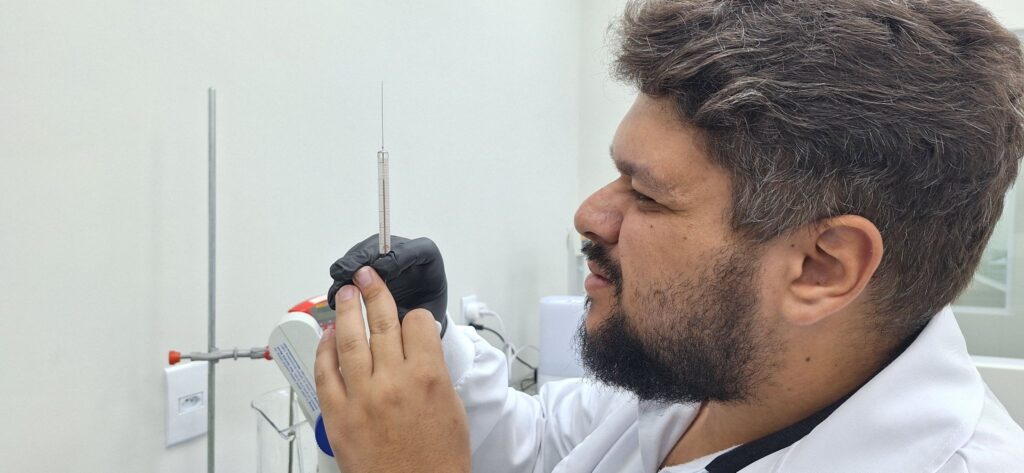 Técnico de laboratório com luvas de proteção inspecionando a medição de precisão em instrumento volumétrico para calibração de líquidos.