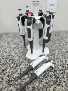 Suporte carrossel com micropipetas monocanal organizadas sobre bancada de granito prontas para testes de calibração volumétrica.