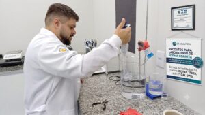 Analista em laboratório operando cromatógrafo a gás em bancada, ao lado de banner e certificado de acreditação ISO/IEC 17025 do Inmetro para serviços de calibração.