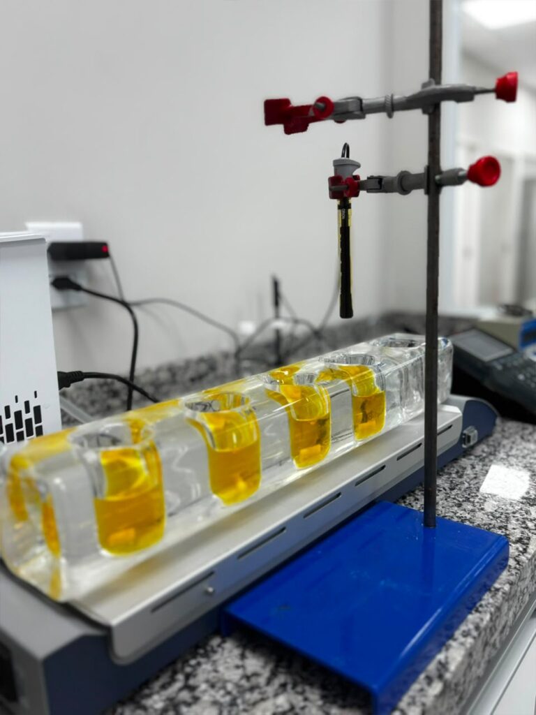 Eletrodo de medição suspenso em suporte universal sobre bloco de amostras para checagens intermediárias e ensaios analíticos em bancada de laboratório.